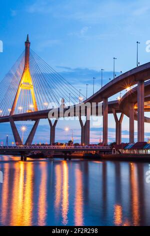 Vue pittoresque sous-jacente de l'échangeur d'autoroute et des ponts suspendus à la tombée de la nuit. Les lumières se reflètent sur la rivière. Thaïlande. Banque D'Images