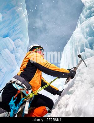 La femme monte une cascade gelée avec une hache de glace en orange veste dans les montagnes Banque D'Images