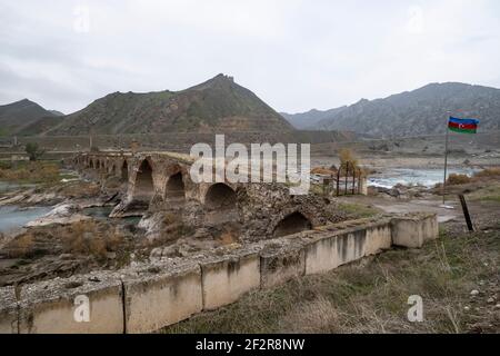 JABRAYIL, AZERBAÏDJAN - DÉCEMBRE 15 : un drapeau national azerbaïdjanais vole à côté du pont de l'arche Khodaafarin du XIIIe siècle reliant les rives nord et sud de l'Aras, situé à la frontière entre l'Azerbaïdjan et l'Iran, le 15 décembre 2020. Khoda Afarin borde un territoire contrôlé par les autorités arméniennes de souche en Azerbaïdjan, à proximité du Haut-Karabakh, qui a été ramené sous le contrôle de l'Azerbaïdjan dans le cadre d'un accord qui a mis fin à la guerre du Haut-Karabakh en 2020. Banque D'Images