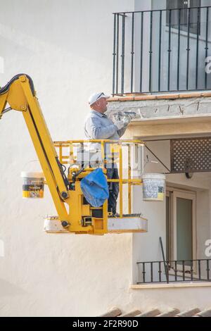 Un constructeur espagnol répare un balcon en se tenant sur un préparateur de cerises. Banque D'Images