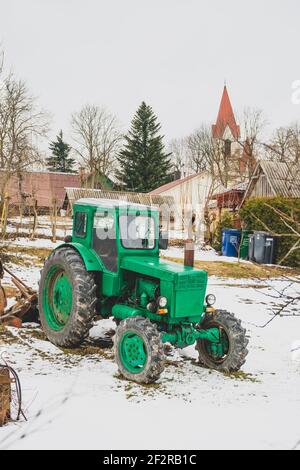 Maison typique en bois dans la campagne avec vieux tracteur vert Belarus dans le jardin en hiver, avec neige. La Biélorussie est une série de tracteurs à quatre roues Banque D'Images