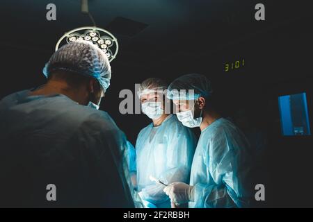 Une équipe professionnelle internationale de chirurgien, d'assistants et d'anesthésiste effectue une opération complexe sur un patient sous anesthésie générale. Sombre Banque D'Images