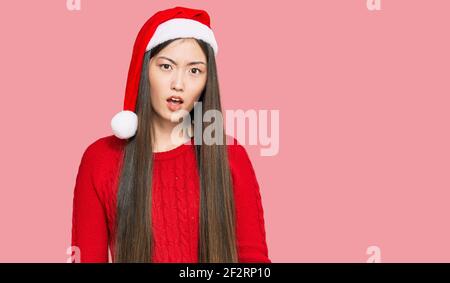 Jeune femme chinoise portant un chapeau de noël dans un visage de choc, regardant sceptique et sarcastique, surpris par la bouche ouverte Banque D'Images