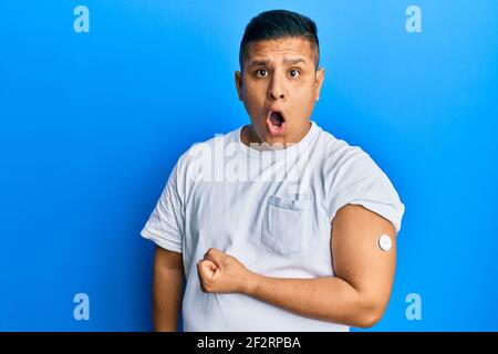 Jeune homme latin utilisant le bouton du glucomètre peur et stupéfait avec la bouche ouverte pour la surprise, incrédulité visage Banque D'Images