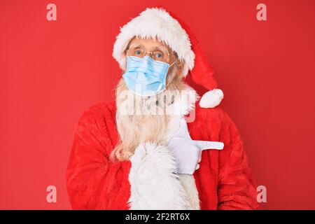 Homme âgé portant le costume du père noël portant un masque de sécurité souriant gai pointant avec la main et le doigt vers le haut côté Banque D'Images