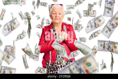 Femme senior belle avec les yeux bleus et les cheveux gris port un style moderne avec une veste en cuir rouge souriante mains sur la poitrine avec les yeux fermés et Banque D'Images