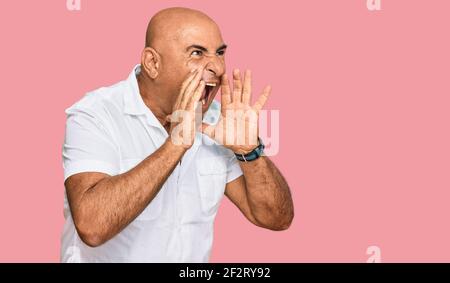 Homme mature du Moyen-Orient avec moustache portant une chemise blanche décontractée crier en colère à voix haute avec les mains sur la bouche Banque D'Images