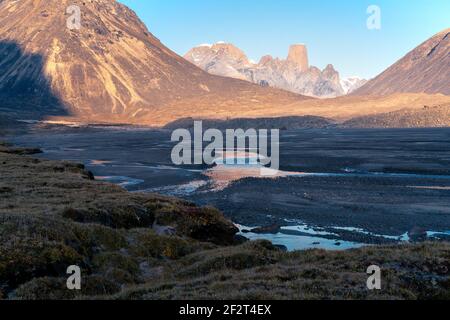 Vents sauvages de rivière à travers le paysage arctique isolé et pierreux. Une grande moraine et des montagnes emblématiques à l'horizon. Mt. Asgard, Col d'Akshayuk, Nunavut, Canada Banque D'Images