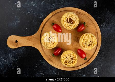 Les pâtes non cuites nichent et les tomates sur une planche en bois Banque D'Images