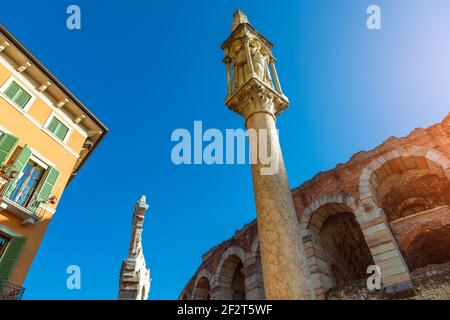 Ville de Vérone, Italie. Partie du mur avec les arches de l'Arena de Vérone (Arena di Verona) et la colonne de Dévotional sur la Piazza Bra sur le ciel bleu avec Banque D'Images