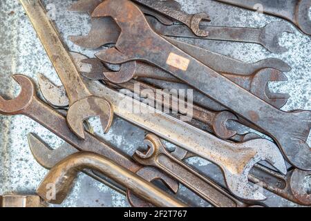 De vieilles clés ouvertes et une clé réglable se chevauchent sur une surface métallique usée, montrant de la rouille, de la corrosion et des traces d'usage en atelier. Banque D'Images