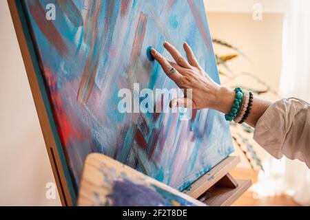 Tableaux abstraits en studio. Femme artiste peinture sur toile à la main et au doigt. Peintre utilisant une compétence et une technique uniques Banque D'Images
