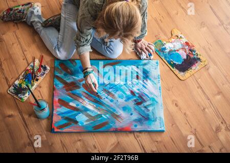 Peinture à l'huile. Artiste assis sur le sol et travaillant sur ses peintures abstraites. Femme peintre dans son studio Banque D'Images