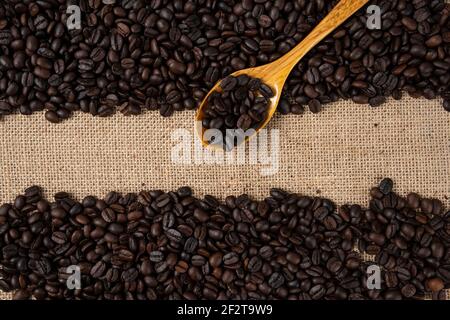 Pile de grains de café torréfiés moyens avec une cuillère en bois parsemée en toile de jute Banque D'Images