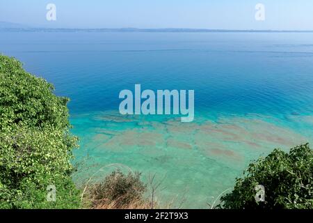 Belle émeraude et eaux calmes du lac de Garde près de la ville de Sirmione, Italie. À l'horizon dans le brouillard le rivage avec de petites villes sur le lac. Banque D'Images