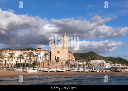 Belle vue sur l'église Sant Bartomeu et Santa Tecla à Sitges avec des bateaux sur la plage sous le beau ciel. Banque D'Images