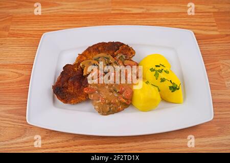 porc pané aux pommes de terre et aux champignons, sauce paprika sur une assiette de service blanche Banque D'Images