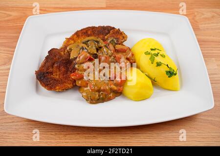 porc pané aux pommes de terre et aux champignons, sauce paprika sur une assiette de service blanche Banque D'Images