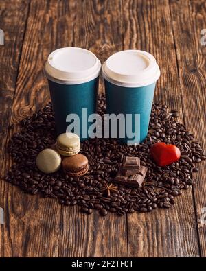 deux tasses en papier de café, macarons, haricots, coeur sur fond de bois Banque D'Images
