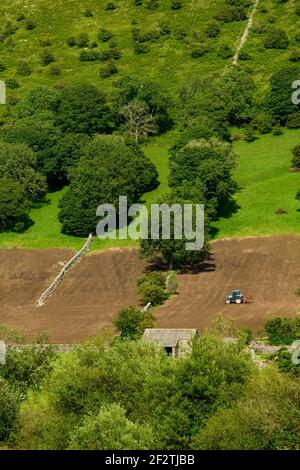 Tracteur travaillant sur de hautes pentes de champs à flanc de coteau escarpés (labourage de terre hereuse pour l'ensemencement) - Wharfe Valley, North Yorkshire, Angleterre, Royaume-Uni. Banque D'Images