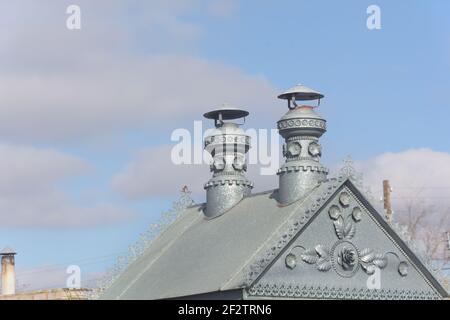 Petit toit en métal avec motifs et tuyaux en fer. Fond bleu ciel. Banque D'Images