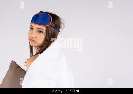 Concept de sommeil sain. Fille endormi bâillant, épuisé, enveloppé dans une couverture et avec un eyemask sur sa tête isolé sur fond gris avec le côté vide Banque D'Images