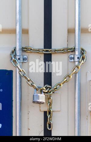 Un cadenas de taille industrielle à usage intensif a été fixé à des chaînes en acier à l'entrée d'un conteneur extérieur qui stocke les outils et l'équipement. Polyvalent i Banque D'Images