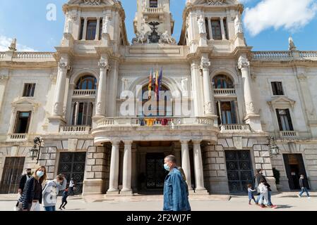 Valence, Espagne. 13 mars 2021. Les personnes portant un masque de visage marchent au-delà de l'hôtel de ville.tous les Fallas Act ont été suspendus de façon permanente en raison de la situation sanitaire causée par Covid19. Pour se souvenir de l'esprit des Fallas pendant la semaine suivante, un chaudron a été allumé comme un rappel sur la place de l'hôtel de ville de Valence. Crédit : SOPA Images Limited/Alamy Live News Banque D'Images