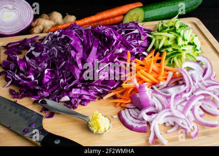 Ingrédients d'une planche à découper en bambou : chou, carottes, concombres et oignons déchiquetés sur une planche à découper en bois Banque D'Images