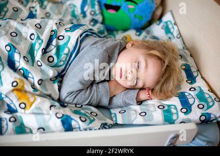 Petit enfant, joli garçon blond, dormant dans un lit bébé l'après-midi avec un petit chien maltais sur le côté Banque D'Images