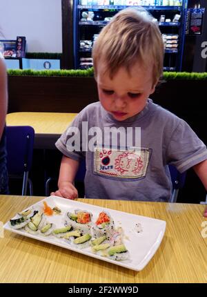 Un petit garçon (2 ans) je regarde de manière suspecte un plat de sushis dans un restaurant Banque D'Images