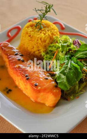 Saumon avec sauce aux fruits de la passion, riz et salade verte sur une assiette blanche. Une alimentation saine. Banque D'Images