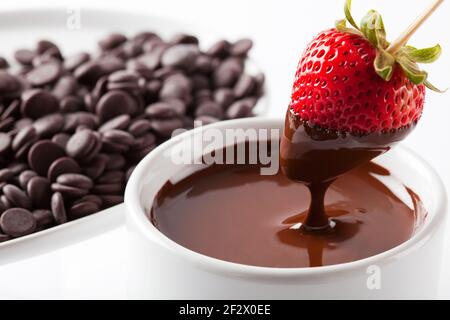 Fraise étant trempée dans le chocolat noir isolé en studio avec arrière-plan blanc Banque D'Images