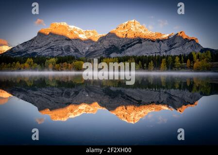 Un soleil chaud illumine le mont Kidd en arrière-tombant et réfléchissant au large de l'étang STILL Wedge dans le pays de Kananaskis, Canada. Banque D'Images