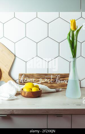 Vue de l'intérieur. Maison douce maison signe manuscrit sur le comptoir de cuisine à côté d'un bol en bois avec oeufs de Pâques et tulipe jaune dans vase et planches à découper Banque D'Images