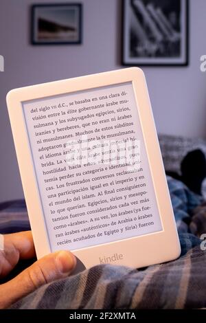 Homme main tenant le lecteur d'ebook kindle blanc dans le lit Banque D'Images