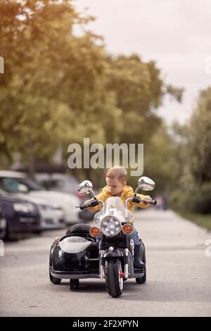 enfant caucasien assis sur une réplique de moto. jouet électrique Banque D'Images