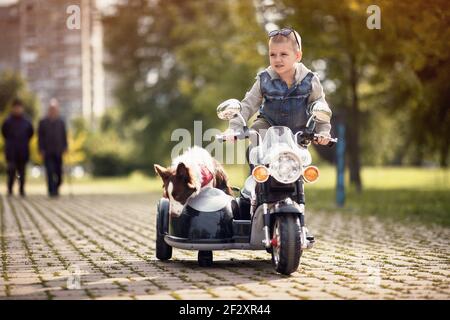 petit garçon debout sur un jouet de moto avec un side-car et un chien dans elle Banque D'Images