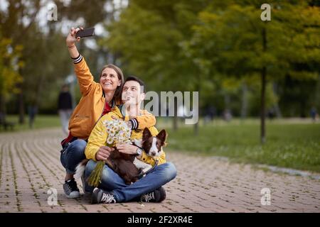 un jeune couple caucasien prend le selfie avec son chien sur un tour, assis sur un chemin dans le parc Banque D'Images