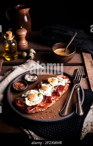 Pain grillé appétissant servi avec du prosciutto et des œufs de caille frits pour le petit déjeuner sur une table rustique en bois Banque D'Images