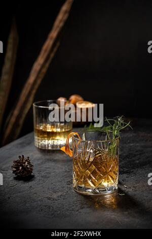 Verre de cristal de whisky à l'ancienne garni de fraîcheur zeste de romarin et d'orange sur une table noire Banque D'Images