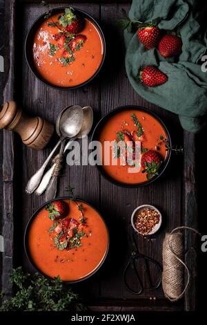 Composition avec vue de dessus et délicieux gazpacho aux tomates et aux fraises maison soupe servie dans des bols sur une table rustique en bois Banque D'Images