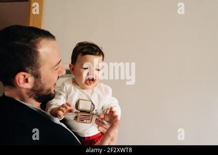 Joyeux jeune père tenant adorable drôle de fils sur les mains pendant s'amuser ensemble dans une pièce lumineuse Banque D'Images