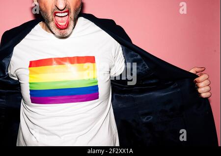 Court inreconnaissable homme à barbe confiante avec des lèvres rouges criant et Démonstration du drapeau LGBT sur un t-shirt blanc sur fond rose Banque D'Images