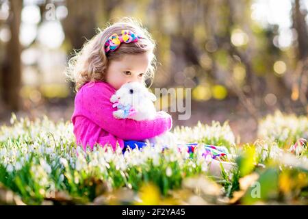 Enfant jouant avec un lapin blanc. Petite fille nourrissant et pétant lapin blanc. Fête de Pâques. Chasse aux œufs avec un enfant et un animal de compagnie. Banque D'Images