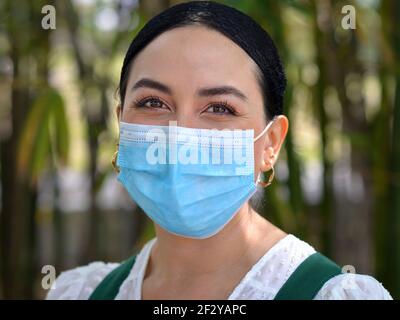 La jeune femme mexicaine sourit avec ses beaux yeux bruns et porte un masque chirurgical jetable bleu clair pendant la pandémie du coronavirus. Banque D'Images