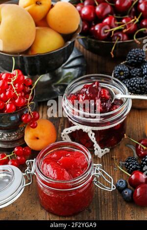 Pots de confiture de fraises de cerise parmi les fruits d'été et d'automne sur une table en bois. Banque D'Images
