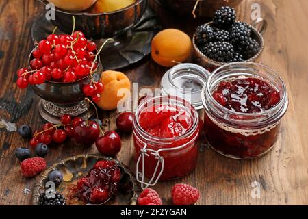 Pots de confiture de fraises de cerise parmi les fruits d'été et d'automne sur une table en bois. Banque D'Images