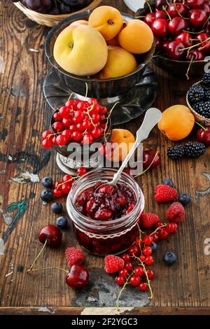 Pots de confiture de fraises de cerise parmi les fruits d'été et d'automne sur une table en bois. Banque D'Images