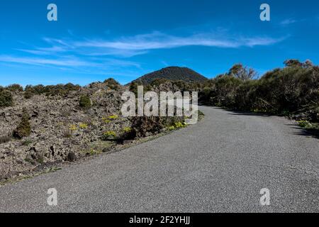 La route sinueuse en Sicile traverse le paysage volcanique de la vieille lave écoulement et vieux cône de volcan couvert d'arbres contre Ciel bleu dans le parc Etna Banque D'Images